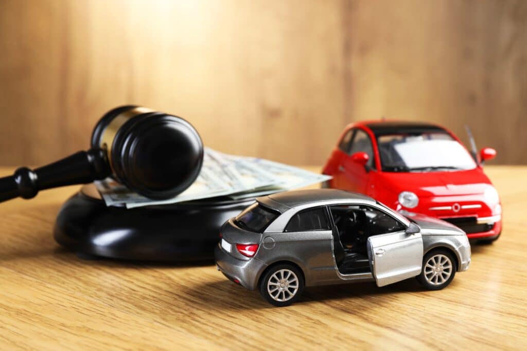 Two toy cars on a desk next to a gavel and money