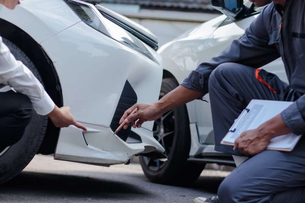 Two cars look to be in an accident. Two people talking one holding a clipboard with paperwork