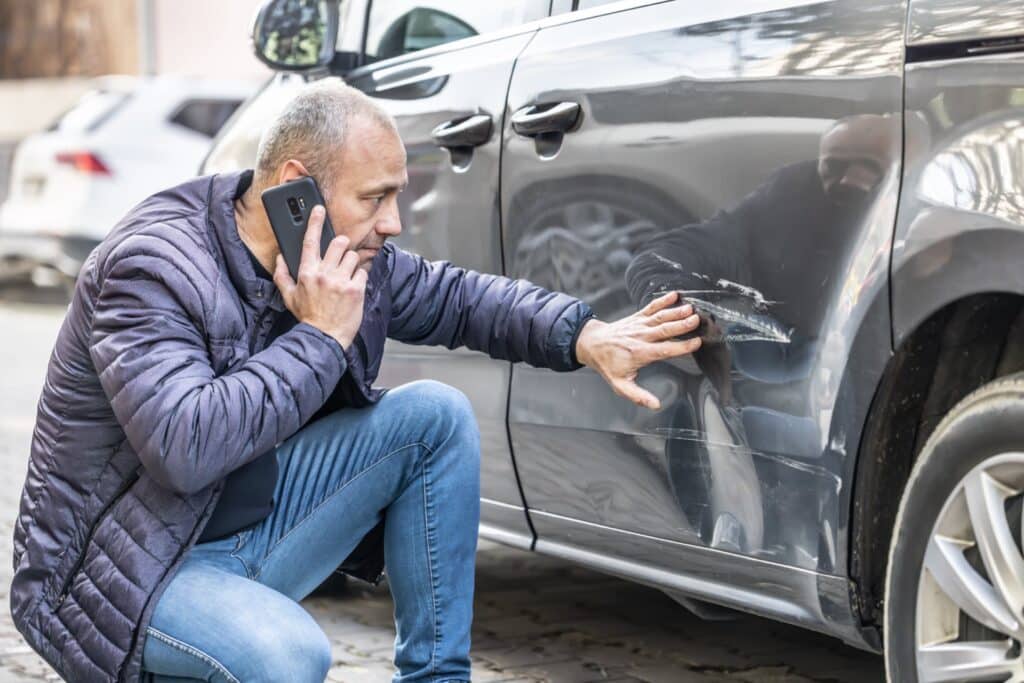 Man on the phone looking at damage done to a car