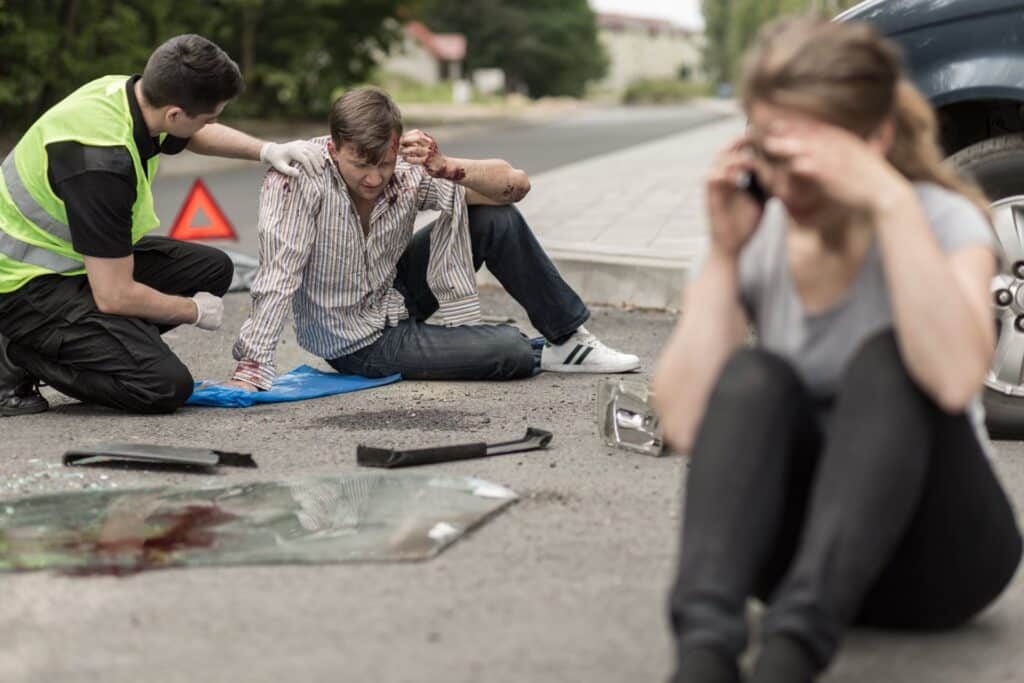 Two people sitting in the road after an accident with debris all over